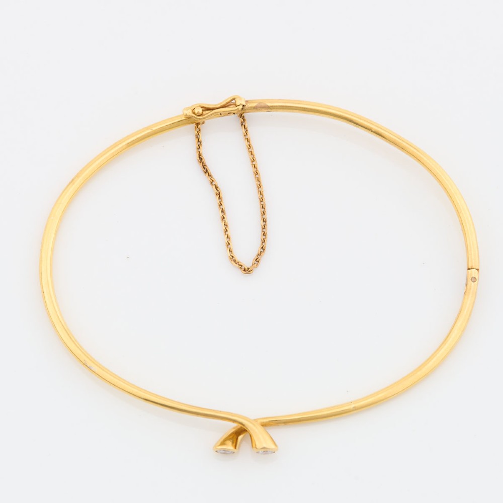 A slim 18ct yellow gold crossover bangle featuring two bezel-set diamonds at the open ends and an attached safety chain. View III