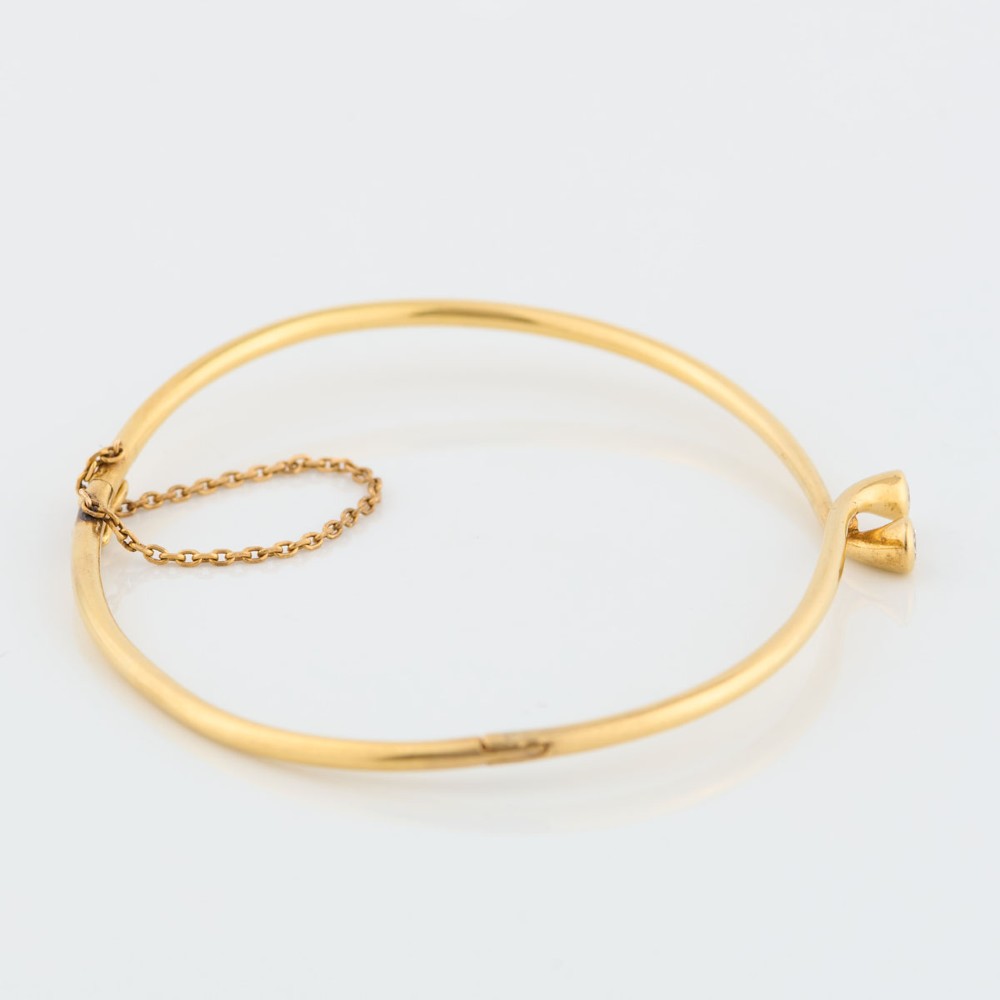 A slim 18ct yellow gold crossover bangle featuring two bezel-set diamonds at the open ends and an attached safety chain. View IV