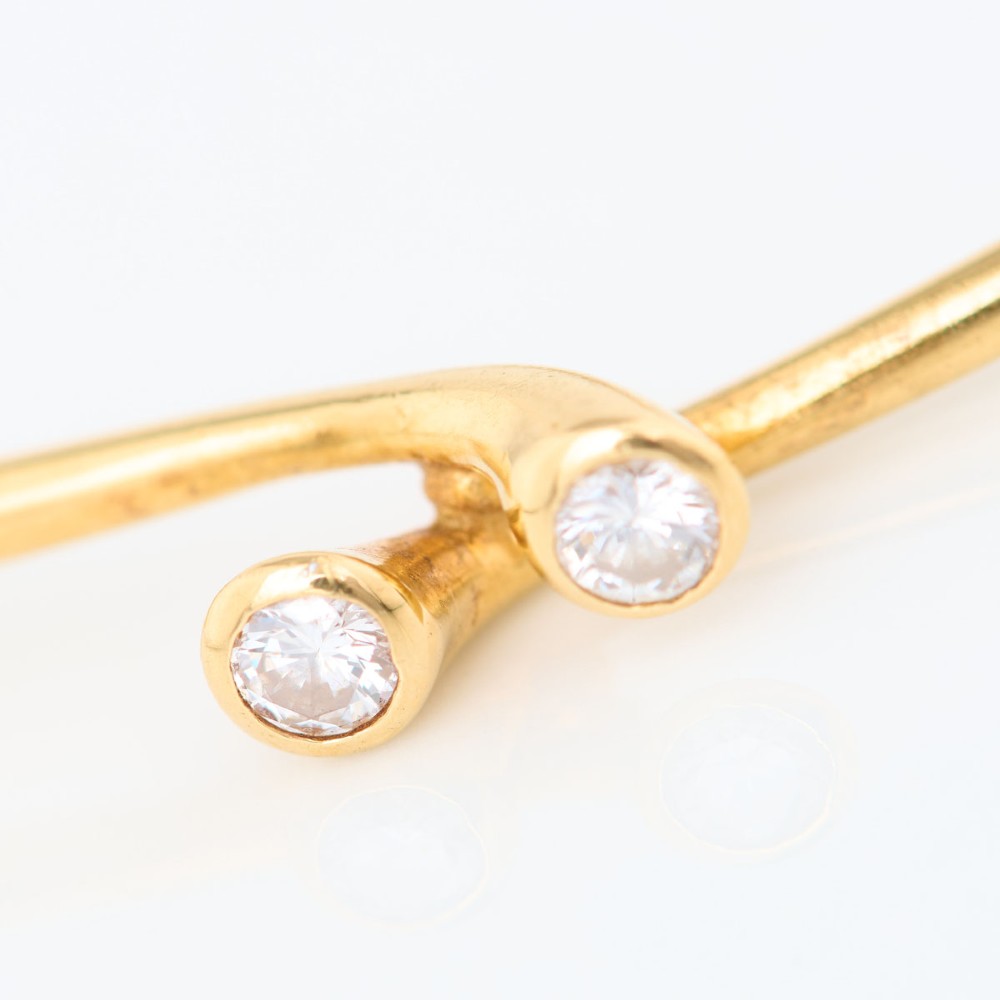 A slim 18ct yellow gold crossover bangle featuring two bezel-set diamonds at the open ends and an attached safety chain. View V