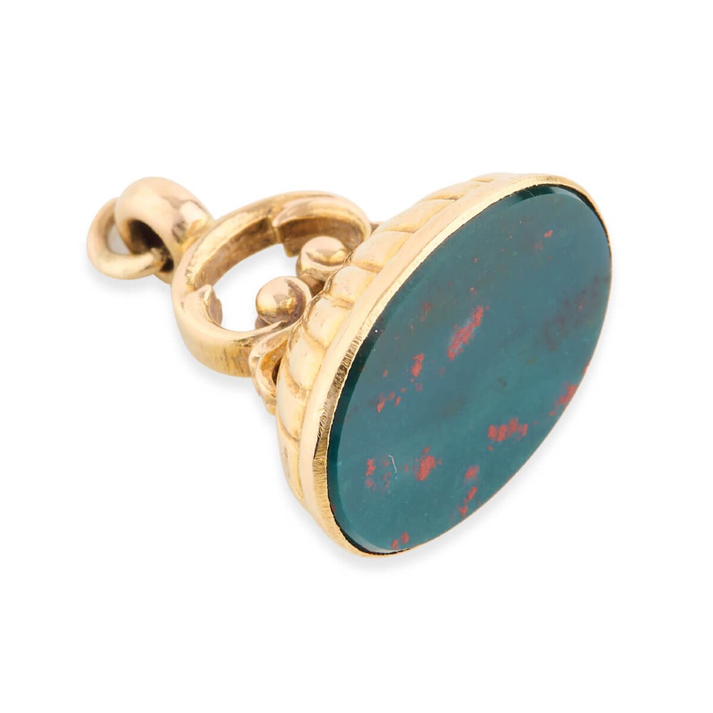 An antique 9ct gold fob mount holding a polished oval green bloodstone with red flecks, featuring fluted rim detail and an arched suspension bail.