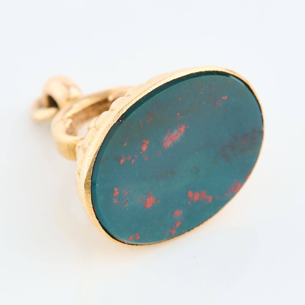 An antique 9ct gold fob mount holding a polished oval green bloodstone with red flecks, featuring fluted rim detail and an arched suspension bail. View V