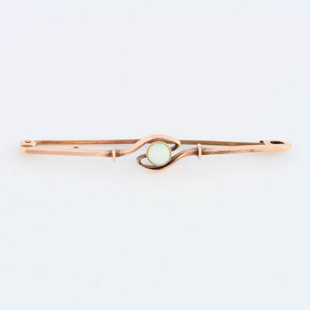 A 9ct yellow gold bar brooch featuring a central round cabochon opal in a bezel setting with a swirl wire accent. View II