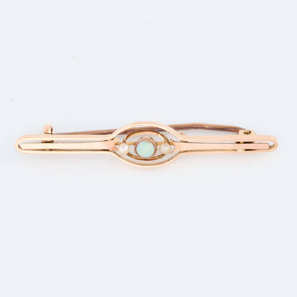 A 9ct gold bar brooch featuring a central cabochon opal flanked by two small seed pearls within an openwork oval motif. View II