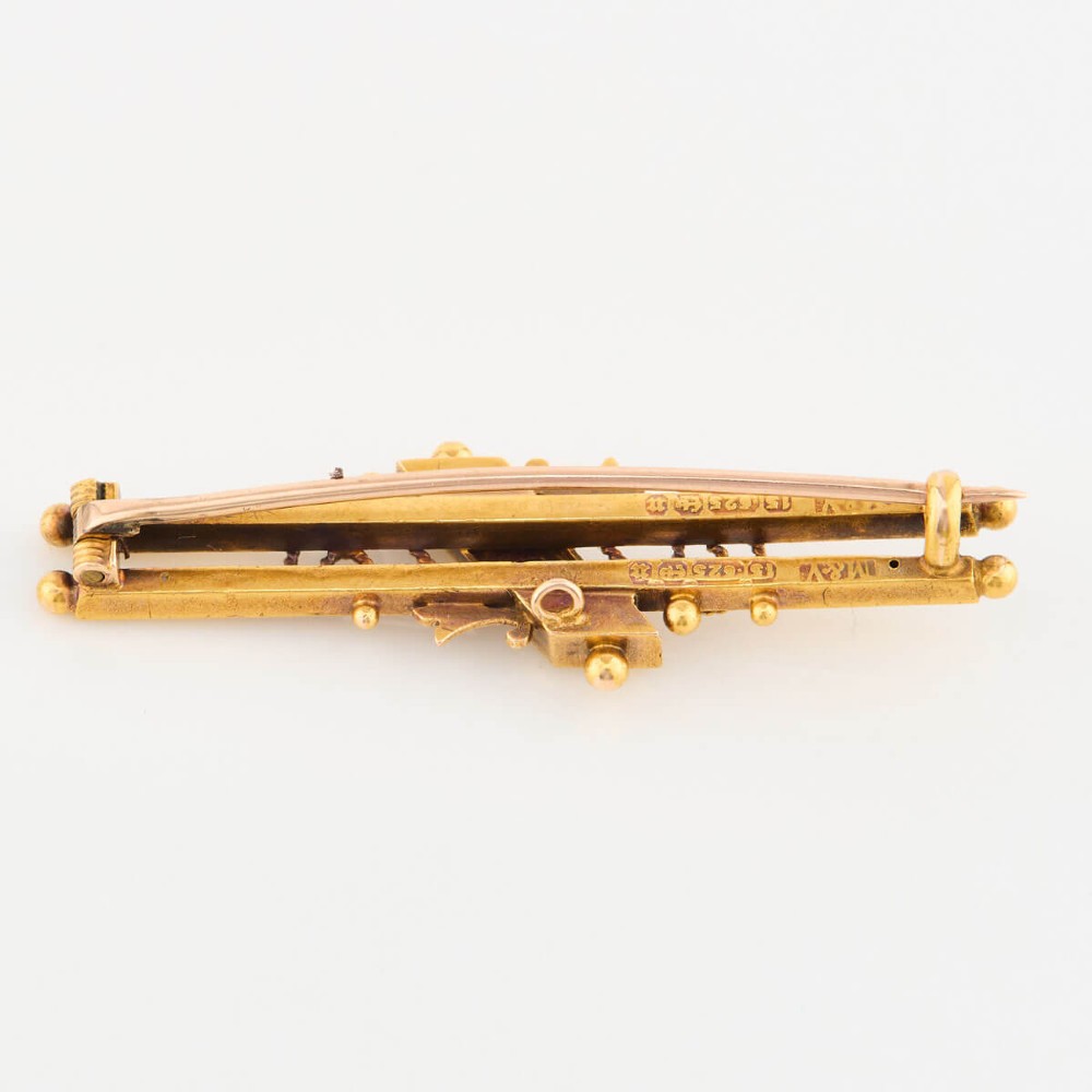 A late Victorian 15ct gold double bar brooch featuring a central lozenge setting with a round blue sapphire flanked by two pearls, decorated with rope-twist wirework and ball finials. View VI