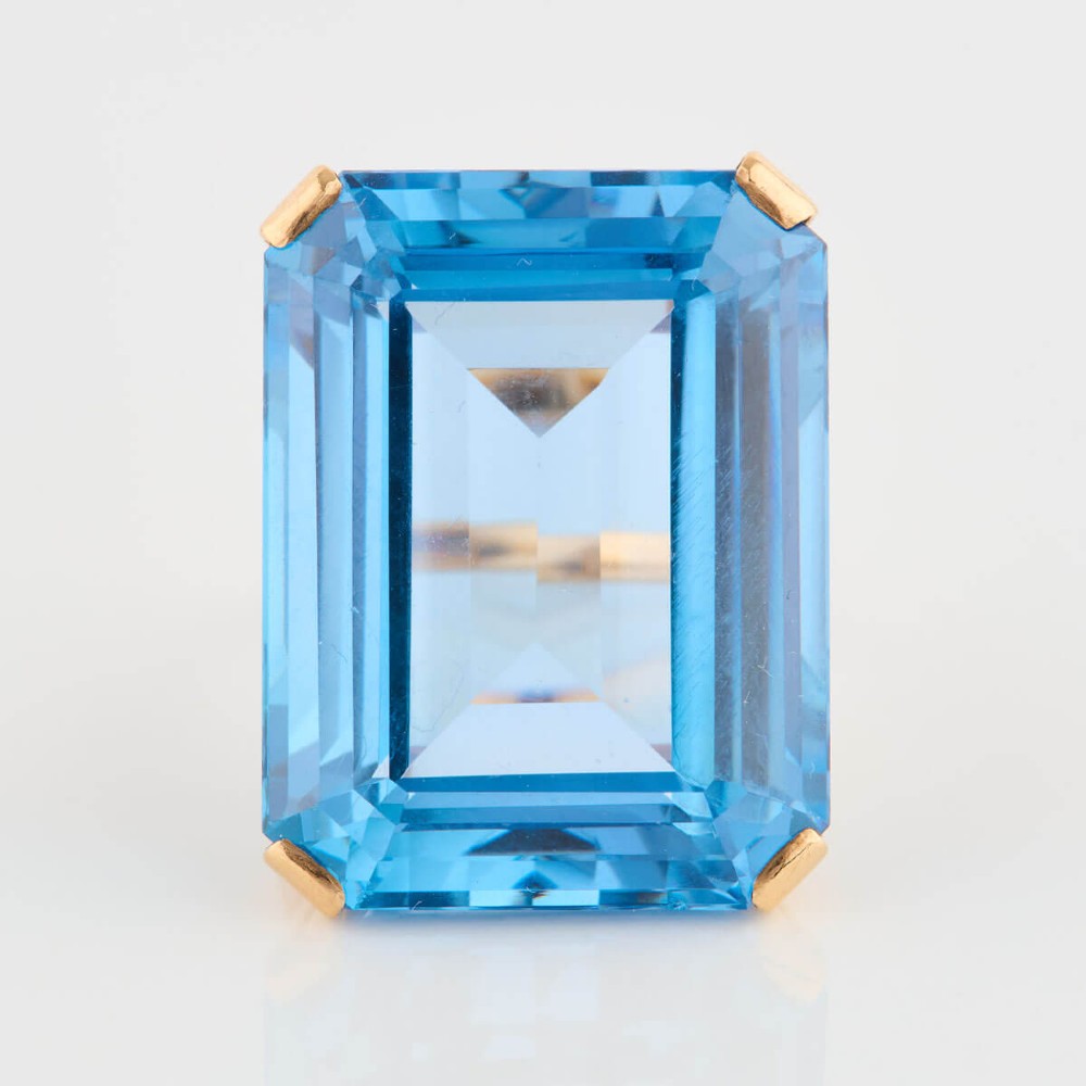 A 9ct gold vintage dress ring featuring a large emerald-cut light blue paste stone held in a raised basket setting. View IV