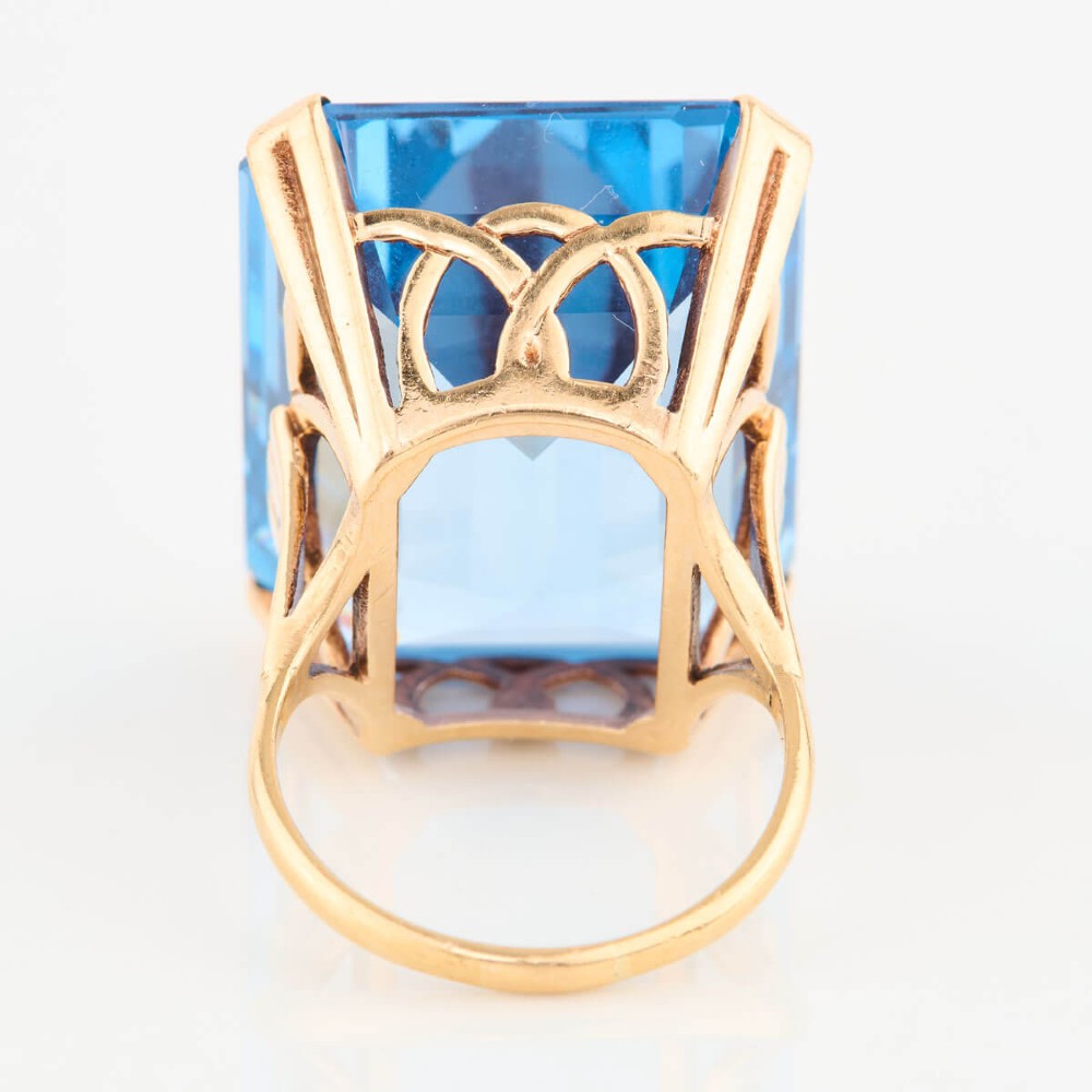 A 9ct gold vintage dress ring featuring a large emerald-cut light blue paste stone held in a raised basket setting. View V