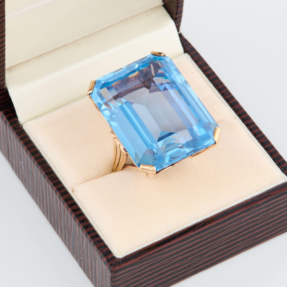 A 9ct gold vintage dress ring featuring a large emerald-cut light blue paste stone held in a raised basket setting. View VII