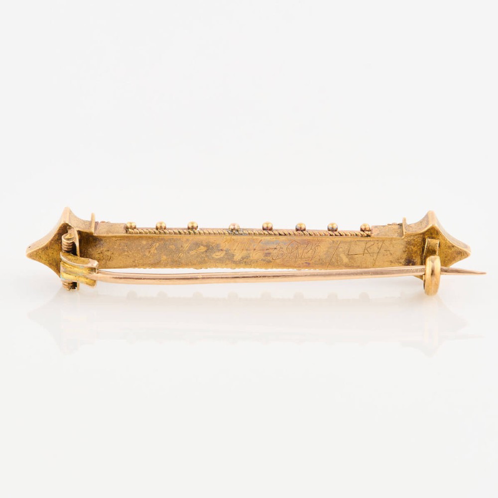 An 18ct yellow gold bar brooch decorated with a row of pearls, beaded borders, and architectural finials. View IV