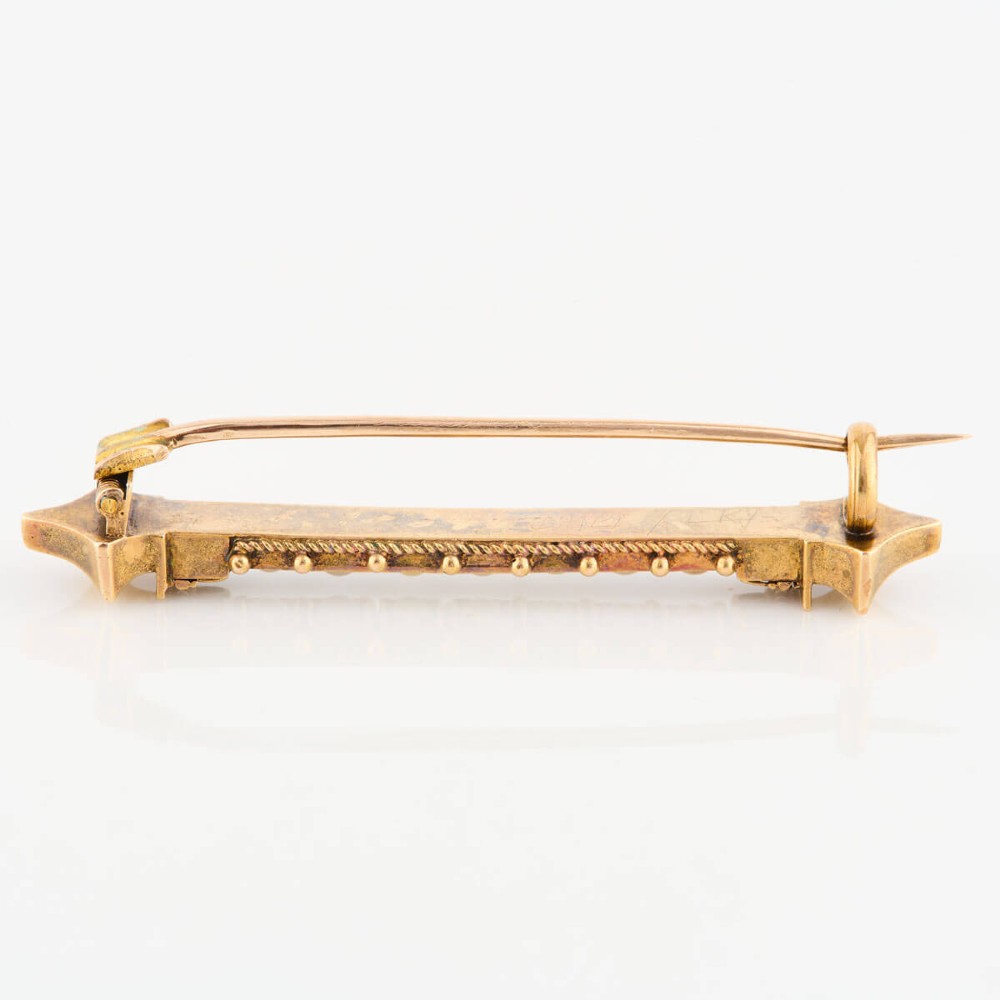 An 18ct yellow gold bar brooch decorated with a row of pearls, beaded borders, and architectural finials. View V