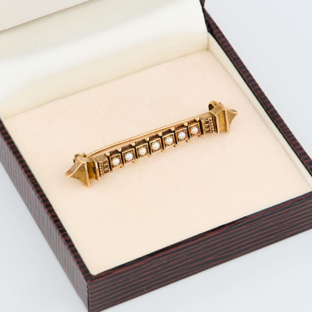 An 18ct yellow gold bar brooch decorated with a row of pearls, beaded borders, and architectural finials. View VI
