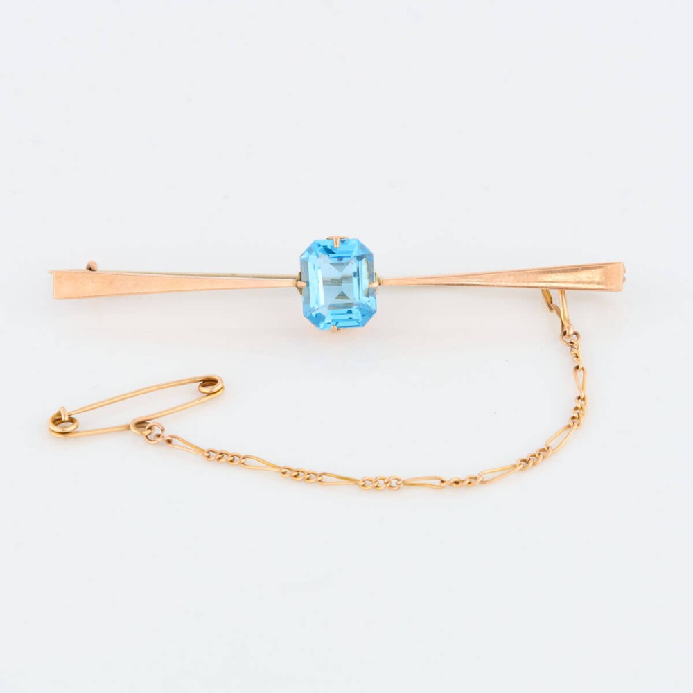 A 9ct yellow gold horizontal bar brooch with a central emerald-cut blue paste stone and an attached safety chain. View III
