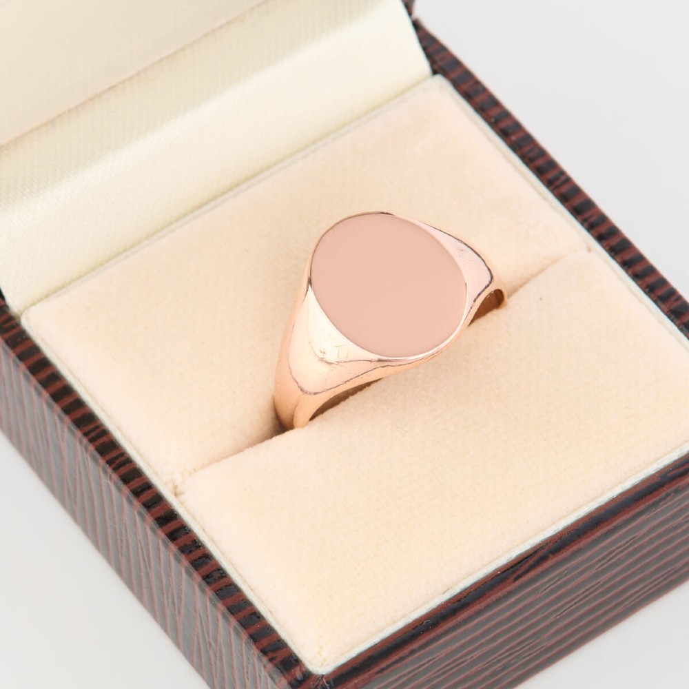 An unengraved 9ct rose gold oval signet ring featuring a polished flat face and thick band. View VII