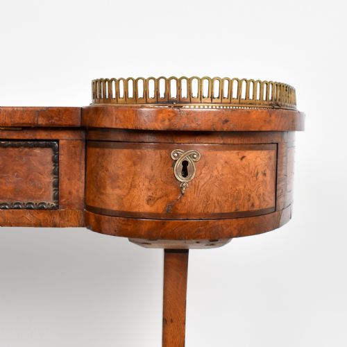fig 2. A Regency period burr oak writing desk featuring a green leather inset top, brass gallery rails on raised side tiers, a central drawer, and trestle legs on brass castors.