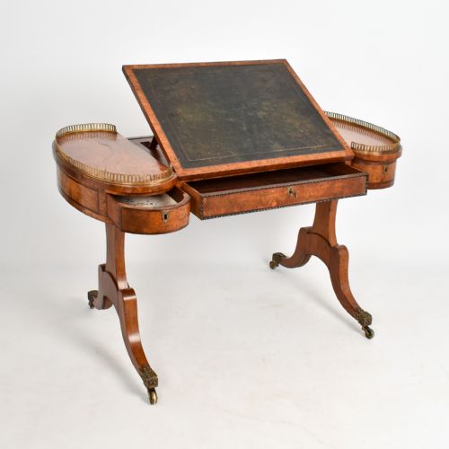 fig 3. A Regency period burr oak writing desk featuring a green leather inset top, brass gallery rails on raised side tiers, a central drawer, and trestle legs on brass castors.