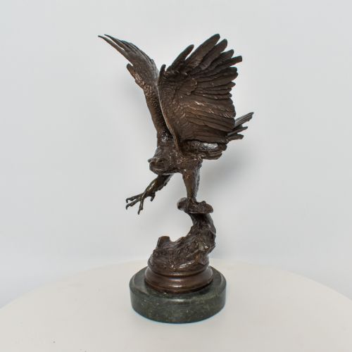 fig 1. A dark brown bronze sculpture depicting an eagle with wings raised perched on a branch, mounted on a round green marble plinth.