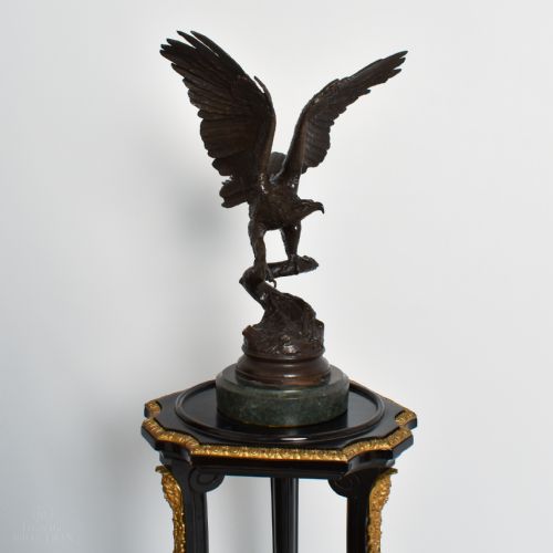 fig 2. A dark brown bronze sculpture depicting an eagle with wings raised perched on a branch, mounted on a round green marble plinth.