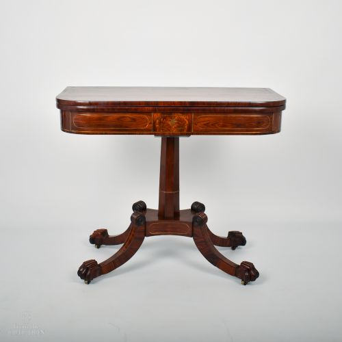 fig 1. A William IV rosewood fold-over tea table featuring a rectangular hinged top, brass inlaid apron, and a central pedestal resting on four carved splayed legs with brass castors.