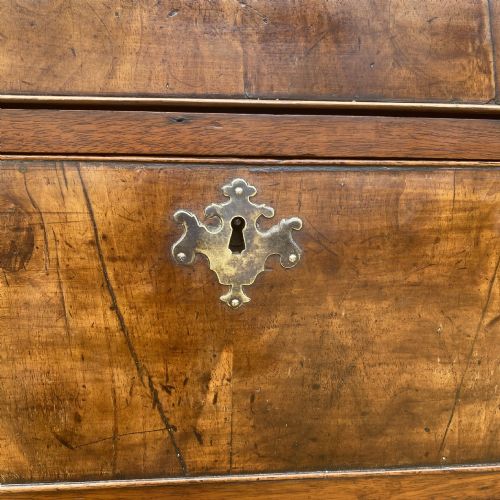 fig 4. A tall George II walnut chest of drawers featuring figured veneer drawer fronts, brass keyhole escutcheons, brass handles, and bracket feet.