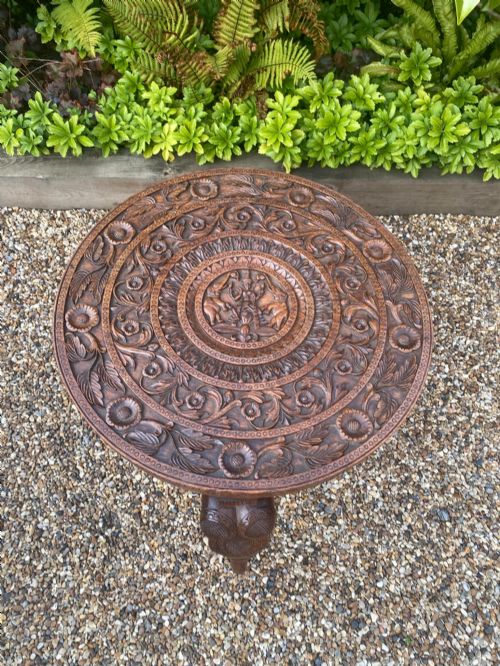 fig 2. A circular carved rosewood side table supported by three legs shaped as detailed elephant heads with trunks extending to the floor.