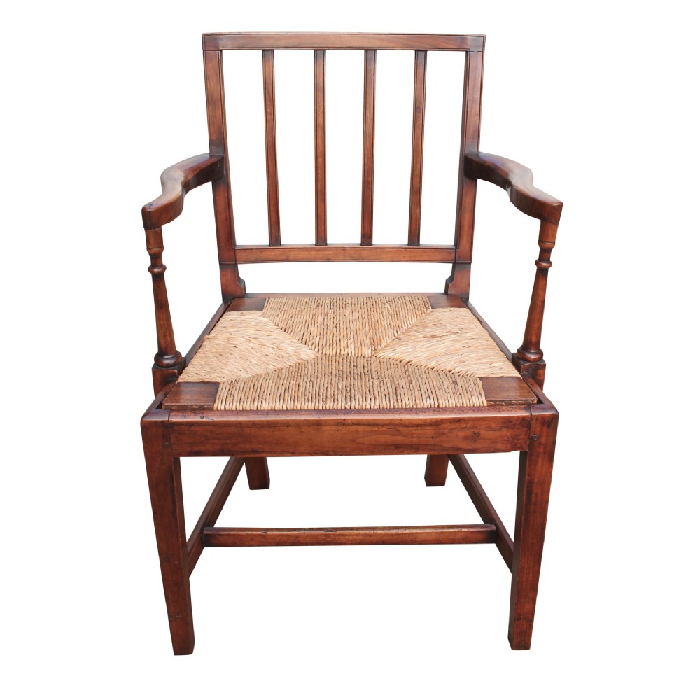 A front-facing view of a dark wooden armchair with a rectangular spindle back, curved armrests, and a woven rush seat.