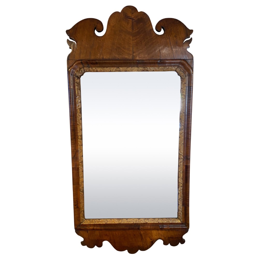 A rectangular George II walnut wall mirror featuring a shaped crest and scroll ears with a gilded inner slip moulding.