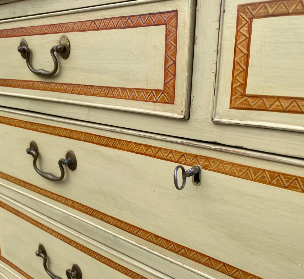A cream-painted Georgian chest of drawers featuring five horizontal drawers with decorative borders and brass swing handles. View IV