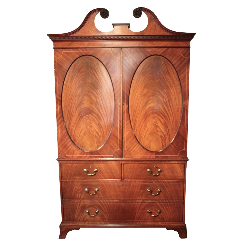 A Georgian mahogany linen press featuring a swan neck pediment, oval inlaid panel doors above a base with four graduating drawers and brass handles.