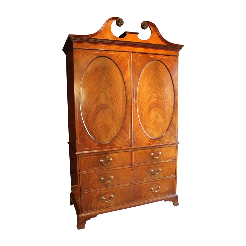 A Georgian mahogany linen press featuring a swan neck pediment, oval inlaid panel doors above a base with four graduating drawers and brass handles. View II