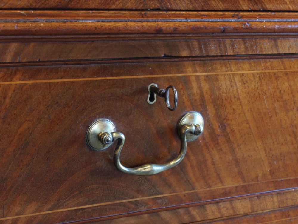 A Georgian mahogany linen press featuring a swan neck pediment, oval inlaid panel doors above a base with four graduating drawers and brass handles. View IV