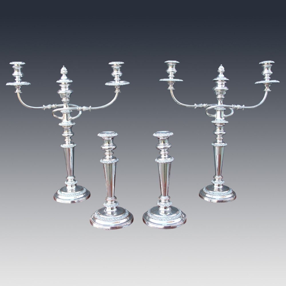 A set of four matching nineteenth-century Sheffield plate candelabras and candlesticks featuring polished silver finishes and classical tiered bases.