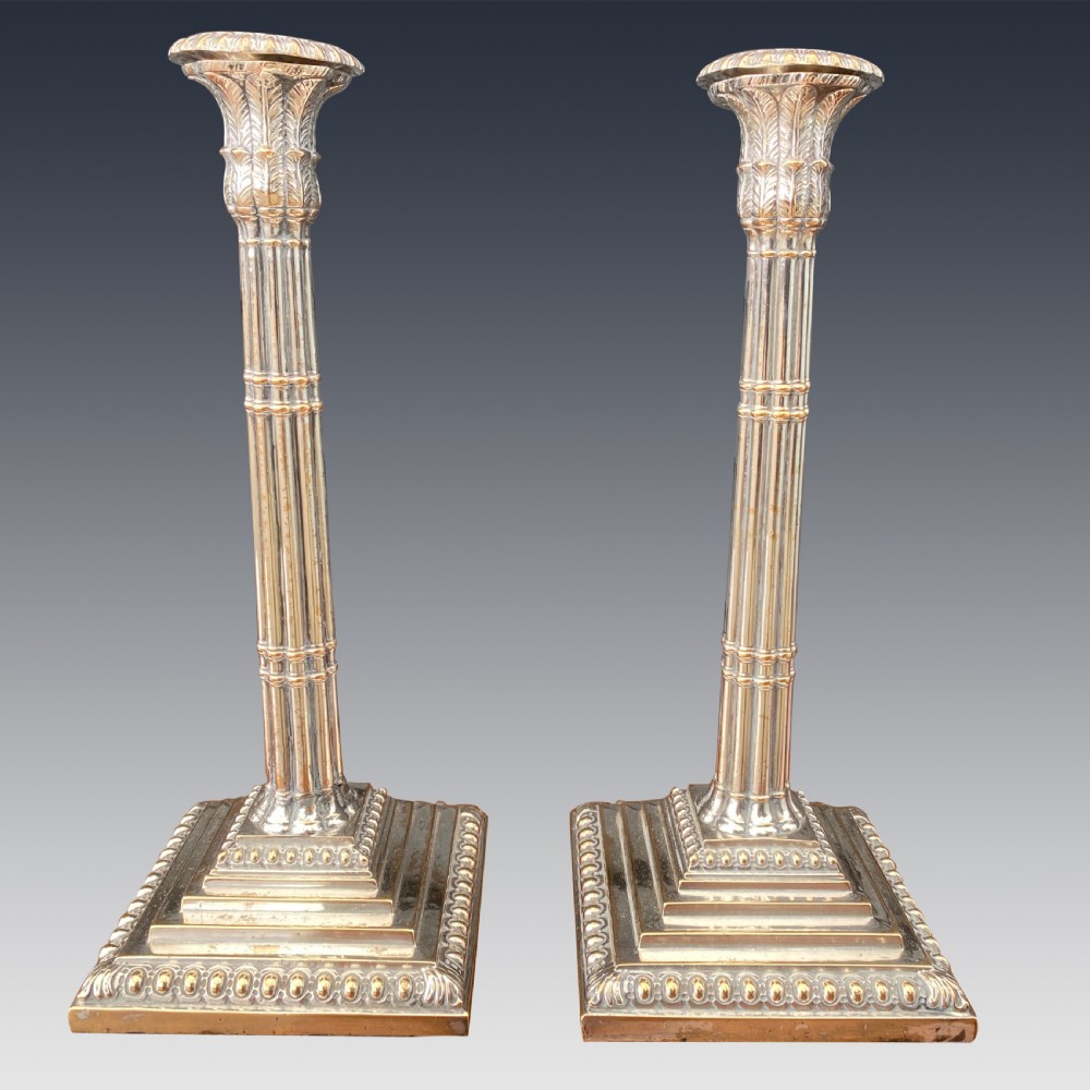 A pair of Georgian Old Sheffield Plate silver candlesticks featuring fluted columnar shafts, acanthus capitals, and stepped square bases with beaded edging.