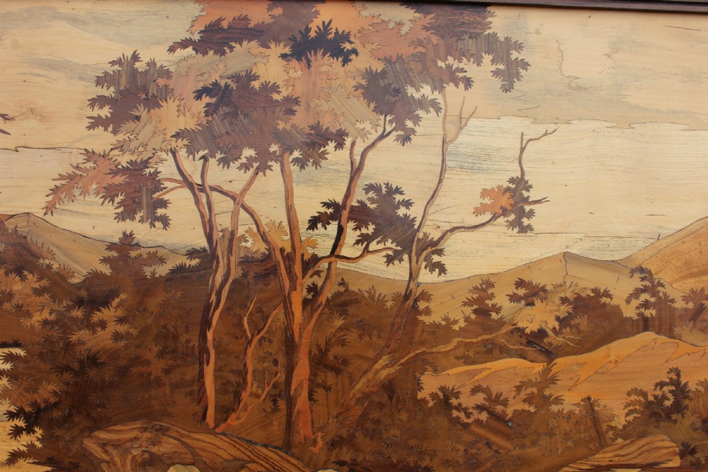 A large rectangular wooden marquetry panel depicting a herd of elephants bathing in a river surrounded by trees and mountains inside a moulded dark wood frame. View III