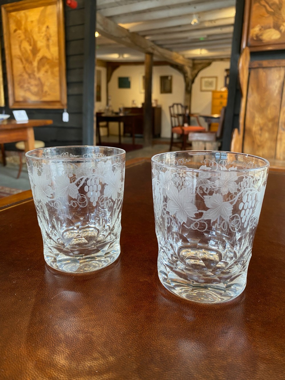 A pair of 19th-century clear hand-blown glass tumblers featuring etched grapevine patterns around the upper rim and facet-cut bases.