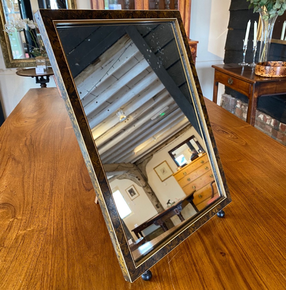 An antique rectangular easel mirror circa 1900 featuring a dark faux-tortoiseshell frame with a gilt inner slip and small ball feet.