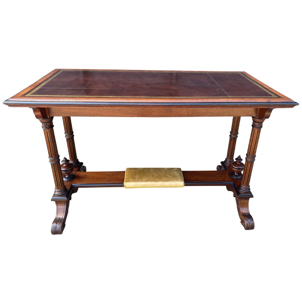 Late nineteenth-century mahogany writing table featuring a dark brown leather inset top with gilded tooling, fluted legs, and a central velvet-padded footrest on a low stretcher.