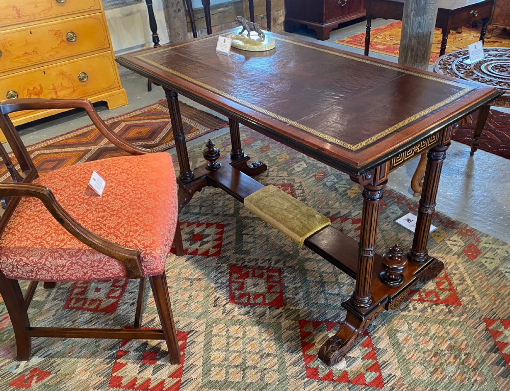 Late nineteenth-century mahogany writing table featuring a dark brown leather inset top with gilded tooling, fluted legs, and a central velvet-padded footrest on a low stretcher. View X