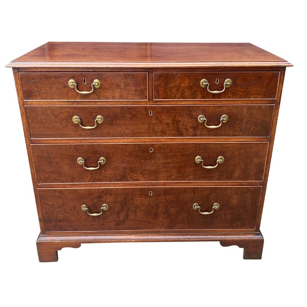 A George III mahogany chest of drawers featuring two short drawers over three long drawers with figured veneers, brass swan-neck handles, and bracket feet.