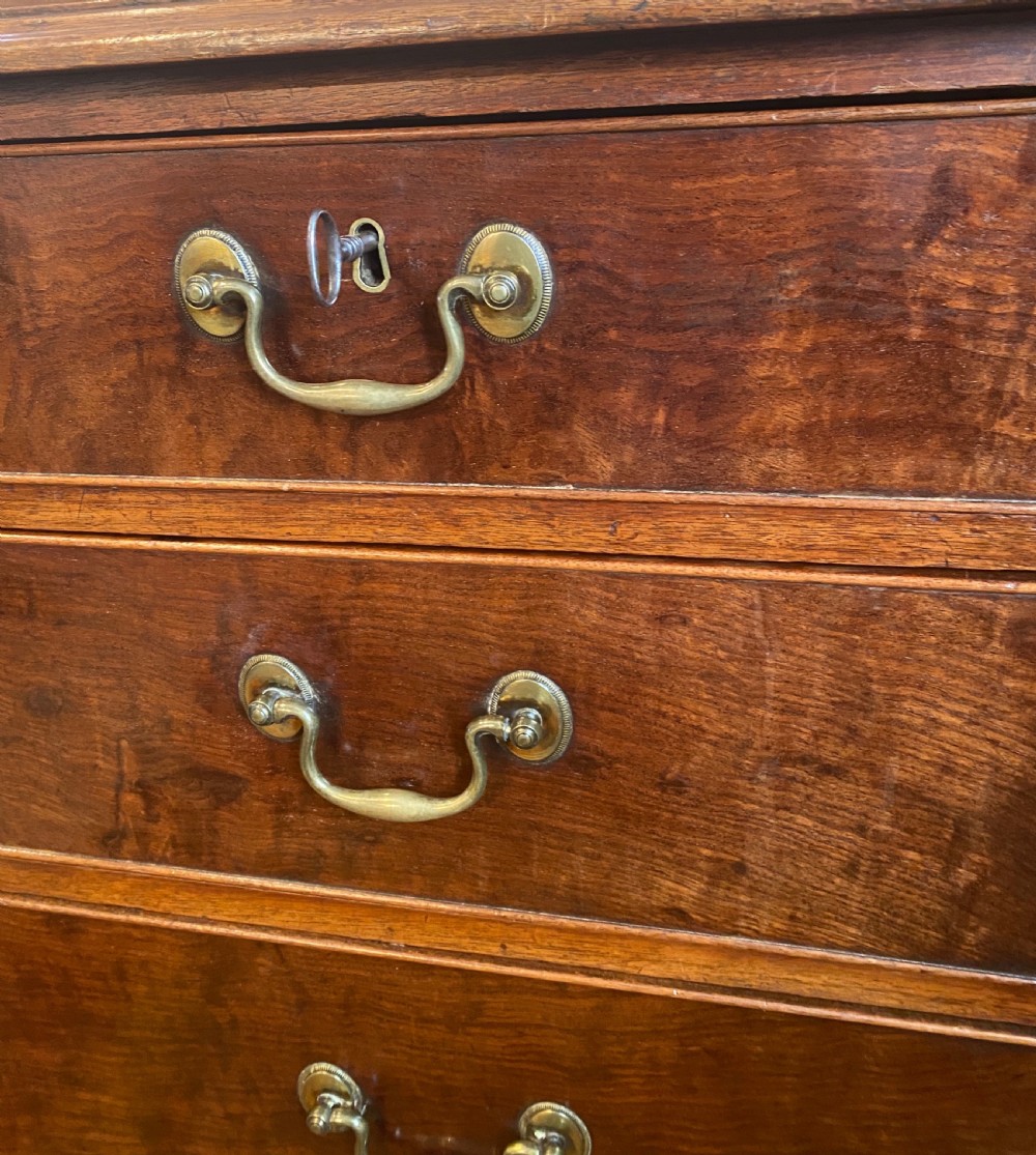 A George III mahogany chest of drawers featuring two short drawers over three long drawers with figured veneers, brass swan-neck handles, and bracket feet. View II