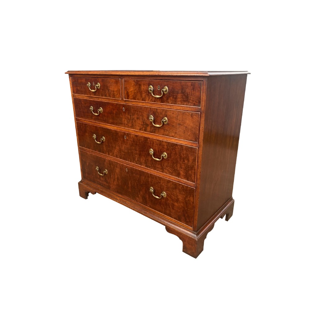 A George III mahogany chest of drawers featuring two short drawers over three long drawers with figured veneers, brass swan-neck handles, and bracket feet. View III