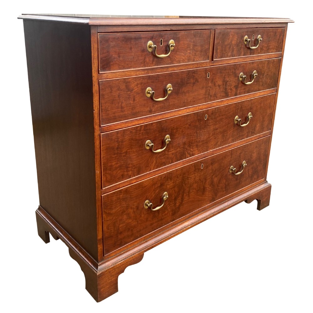 A George III mahogany chest of drawers featuring two short drawers over three long drawers with figured veneers, brass swan-neck handles, and bracket feet. View V