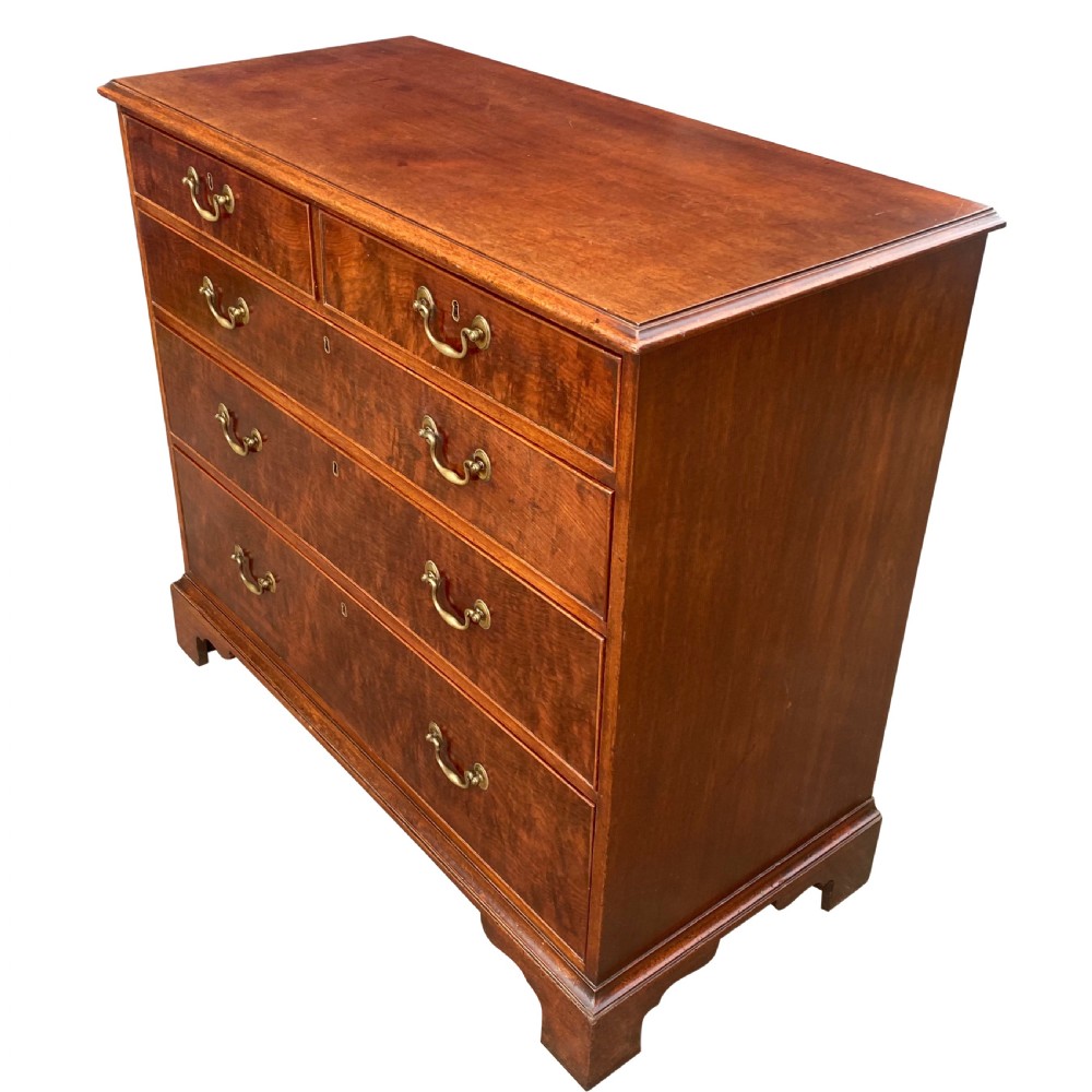 A George III mahogany chest of drawers featuring two short drawers over three long drawers with figured veneers, brass swan-neck handles, and bracket feet. View VI