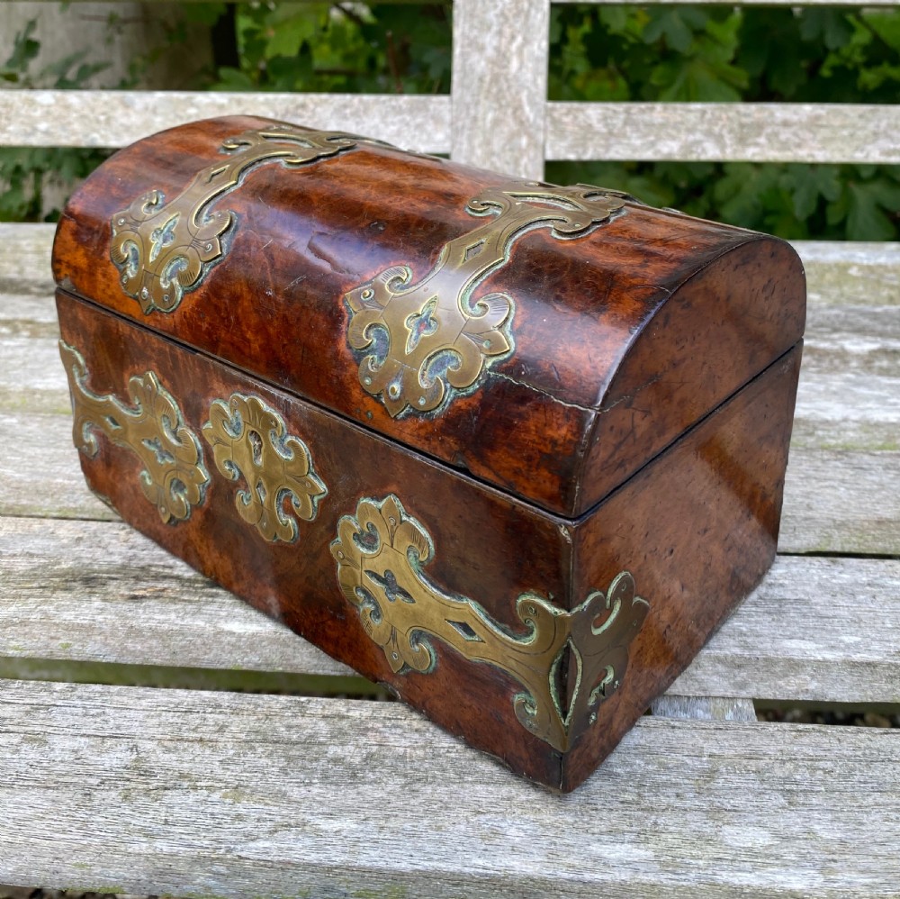 A 19th-century domed amboyna burr wood box featuring decorative brass strapwork mounts and corner fittings.