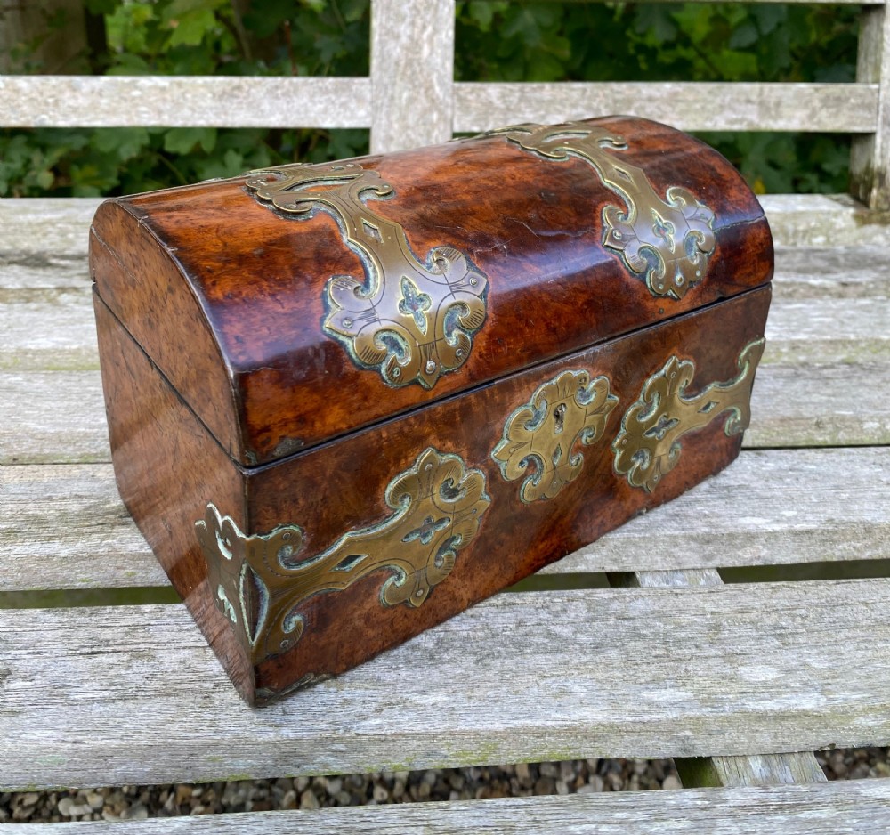 A 19th-century domed amboyna burr wood box featuring decorative brass strapwork mounts and corner fittings. View V