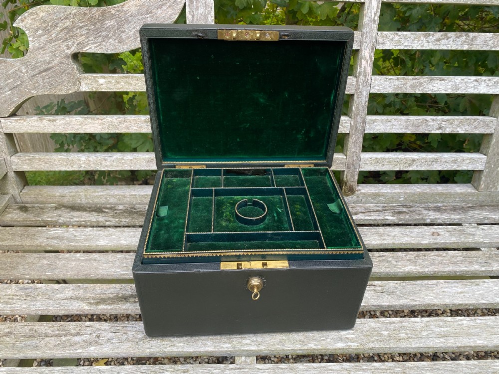 An open 19th-century dark leather jewellery box revealing a green velvet compartmentalised tray and brass lock mechanism.