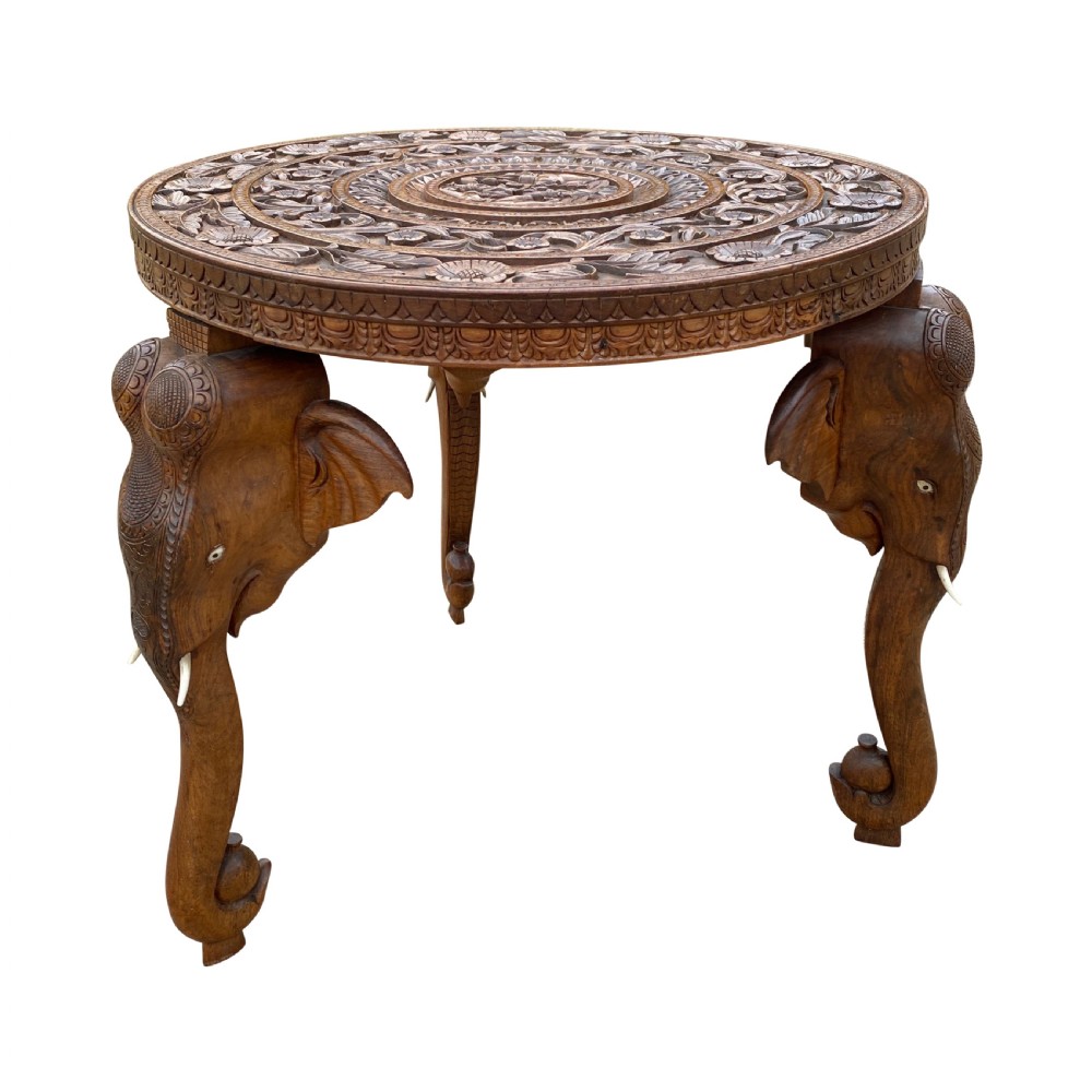 A circular hand-carved rosewood side table with a floral relief surface and three legs shaped as detailed elephant heads with downturned trunks.