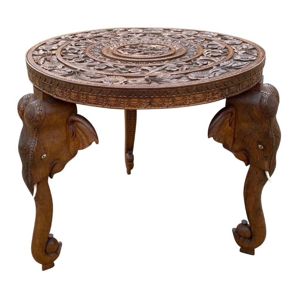 A circular hand-carved rosewood side table with a floral relief surface and three legs shaped as detailed elephant heads with downturned trunks. View II