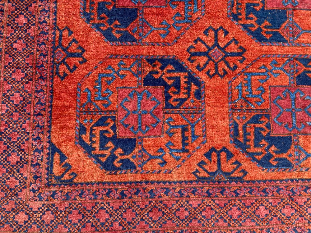 A hand-woven antique Turkmen wool rug featuring a repeating pattern of dark blue octagonal gol motifs on a terracotta red field with a geometric border. View II