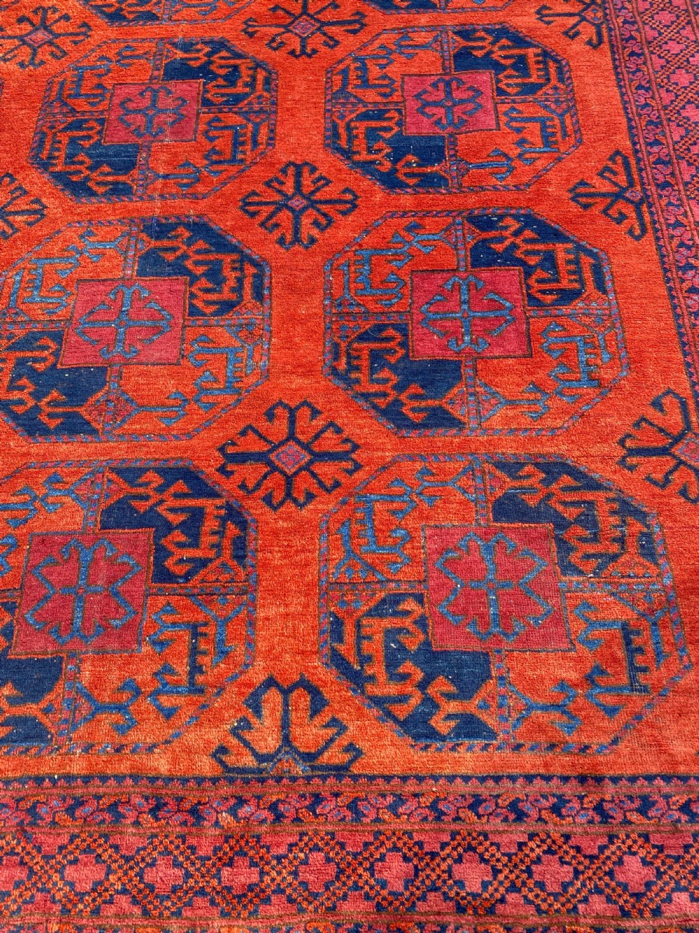 A hand-woven antique Turkmen wool rug featuring a repeating pattern of dark blue octagonal gol motifs on a terracotta red field with a geometric border. View III