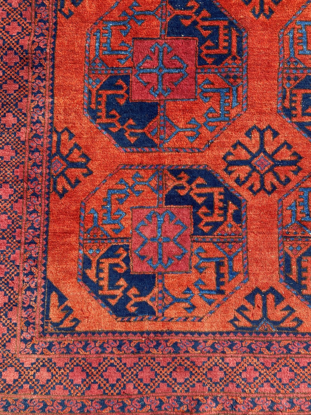 A hand-woven antique Turkmen wool rug featuring a repeating pattern of dark blue octagonal gol motifs on a terracotta red field with a geometric border. View IV