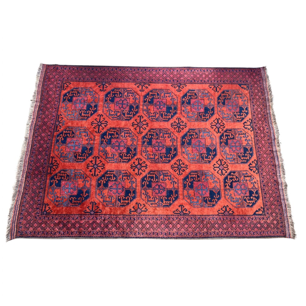 A hand-woven antique Turkmen wool rug featuring a repeating pattern of dark blue octagonal gol motifs on a terracotta red field with a geometric border. View V